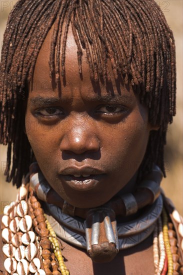 ETHIOPIA, Lower Omo Valley, Tumi, "Hamer Jumping of the Bulls initiation ceremony, Married Hamer lady, her hair greased with ocher colouring and animal fat into plaits known as Goscha. She is wearing a necklace know as a Bignere - an metal band with a phallic protuberance to signify that she is a first wif"