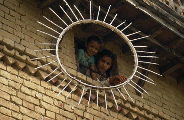 NEPAL, Kathmandu Valley, Children looking out of a window framed by the sun symbol of the Communist Party of Nepal- United Marxist Leninists