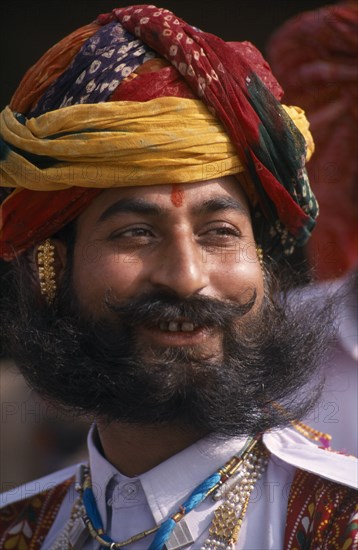 INDIA, Rajasthan, Bikaner, Head and shoulders portrait of a Rajput man smiling with a beard wearing ceremonial dress and a turban at the start of the Camel Festival