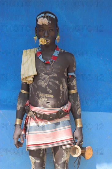 ETHIOPIA, Lower Omo Valley, Key Afir, Tsemay man in traditional attire with flower in mouth at weekly market