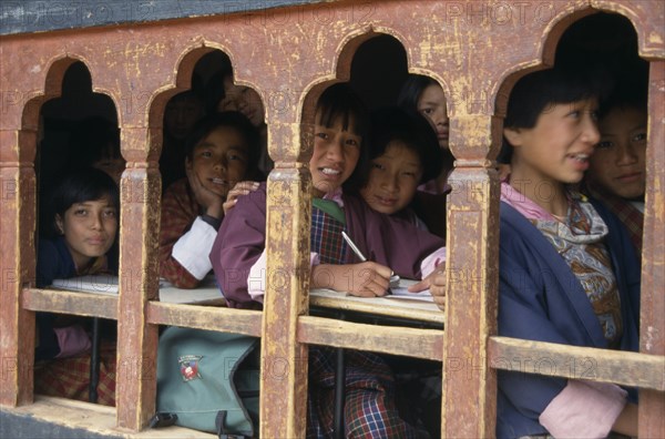 BHUTAN, Thimphu, "School children in class writing at desks framed in line of low set, arched, glassless windows."
