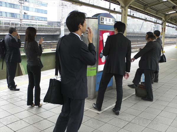 JAPAN, Honshu, Tokyo, "Yurakucho - the smokers corner on the JR train platform, men and young woman smoking"