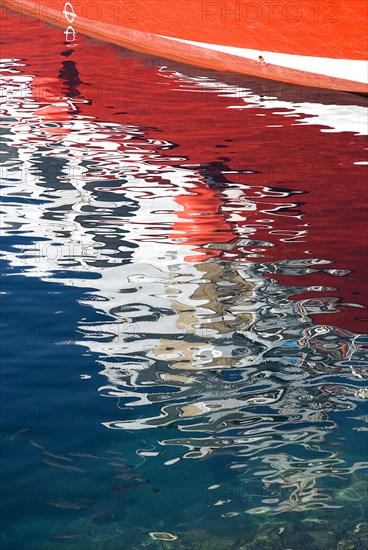 SPAIN, Canary  Islands, Lanzarote, Reflection of red hull of boat in rippled waters of the harbour Puerto del Carmen.