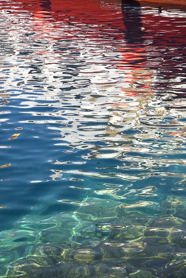 SPAIN, Canary  Islands, Lanzarote, Red and white reflection of boat in rippled water of harbour Puerto del Carmen.