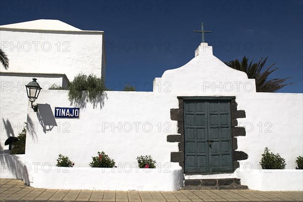 SPAIN, Canary  Islands, Lanzarote, "Tinajo village in island interior.  Section of white painted walls of village church with green painted door, plants and lantern casting strong shadow on wall."