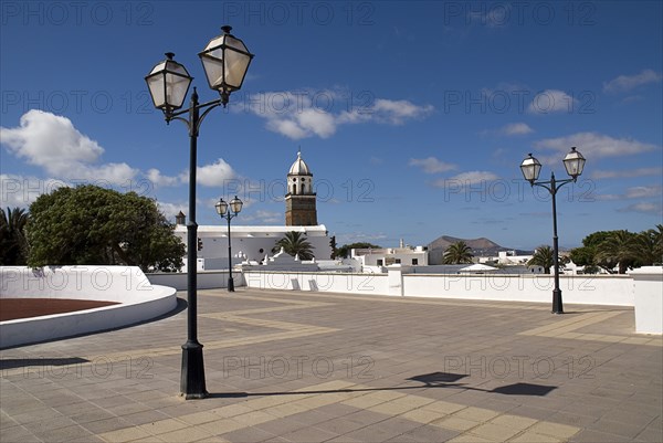 SPAIN, Canary  Islands, Lanzarote, "Teguise, the former capital of the island.  Large open square known as Parque le Mareta with tower of Church of Nuestra Senora de Guadalupe’s and street lamps."