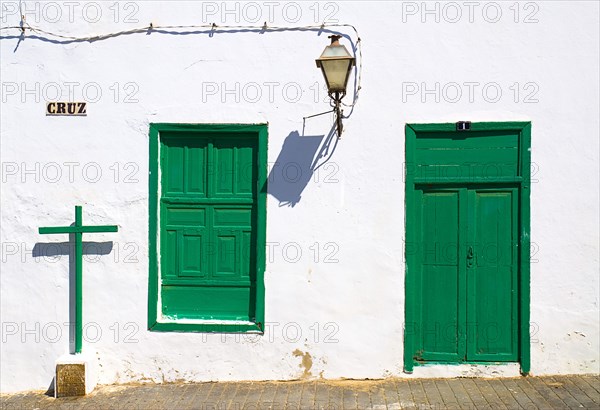 SPAIN, Canary  Islands, Lanzarote, "Teguise, former capital of the island.  Detail of house facade with typical white painted walls and green door and window shutters, cross and lantern cast shadows."