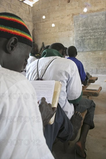 GAMBIA, Western Gambia, Tanji, Tanji Village.  Muslim boys writing in arabic at their desks while attending an islamic religious class at the Ousman Bun Afan Islamic school.  Blackboard on wall in front of them.