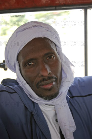 GAMBIA, Atlantic Coast, Banjul, Head and shoulders portrait of African Muslim man travelling on a bus wearing white head-dress and looking direct to camera.