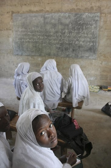 GAMBIA, Western Gambia, Tanji, Tanji Village.  African Muslim girls wearing white headscarves attending a class at the Ousman Bun Afan Islamic school.  Girls in foreground looking back towards the camera.