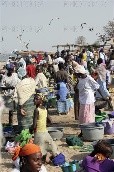 GAMBIA, Western Gambia, Tanji, Busy fish and food market on beach crowded with mostly women and children.  Fishing boats beyond and seagulls overhead.