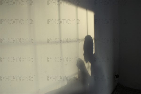 GAMBIA, Western Gambia, Tanji, Tanji Village.  Shadow of man eating and window frame on wall of small restaurant in soft light.  Frame creates the effect of bars or cage and impression of enclosure.