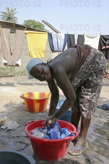 GAMBIA, Western Gambia, Tanji, Young woman bending to wash her family's clothes in a bowl before hanging them outside to dry in the yard of their house.