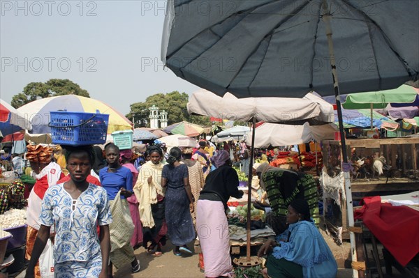 GAMBIA, Western Gambia, Serekunda, "Bakau Market, Atlantic Road.  Busy market scene with women selling fruit and vegetables.  Woman in foreground carrying box on her head."