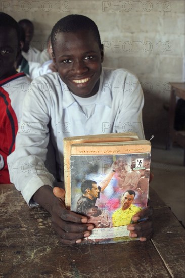 GAMBIA, Western Gambia, Tanji, Tanji village.  Smiling student from Usman Bun Afan private Islamic school proudly showing his exercise book with picture of a football referee showing a yellow card to Brazilian football player Cafu.