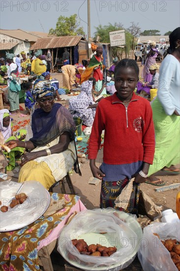 GAMBIA, Western Gambia, Tanji, Tanji market.  Young girl selling sweet snacks at Tanji market with older woman seated at stall beside her.