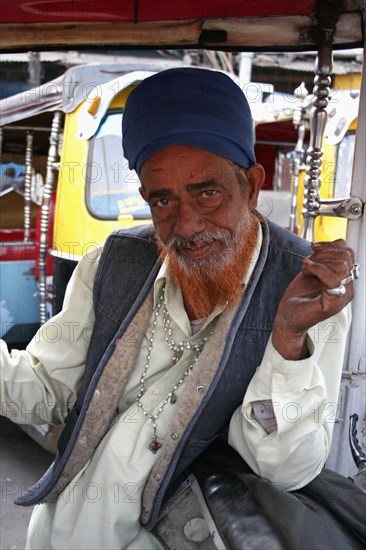 INDIA, Delhi, New Delhi, "Portrait of auto rickshaw driver inside vehicle with red dyed beard, silver rings and necklace."