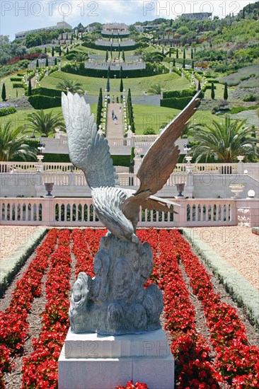 ISRAEL, Northern Coast, Haifa, Zionism Avenue.  Eagle sculpture set in flower bed of scarlet plants at the Baha'i gardens with view over tiered gardens stretching away beyond.