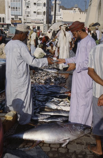UAE, Oman, Muscat, Mutrah fish market.  Male vendor and customer making cash transaction over display of fish laid out on road.