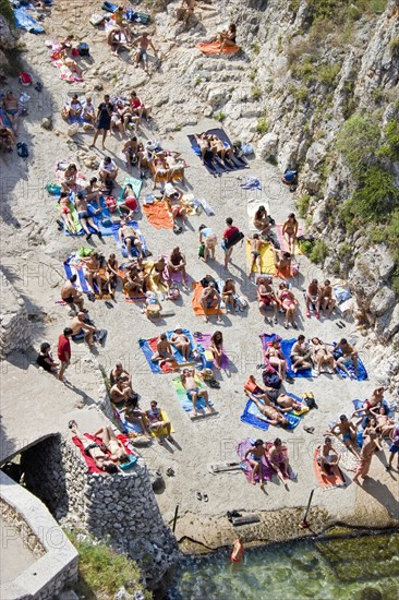 ITALY, Puglia, Lecce, Tricase.  Looking down on people sunbathing on coloured beach towels laid out on rocks next to the sea.