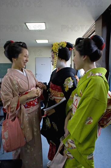 JAPAN, Honshu, Kyoto, "Gion area. Three Maiko or apprentice geisha wearing kimonos, talking and laughing after finishing their classes at Mia Garatso school for Geisha and Maiko."