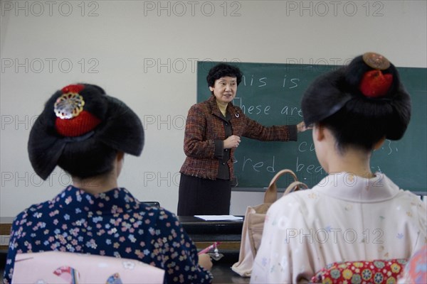 JAPAN, Honshu, Kyoto, "Gion area the neighbourhood where Geisha live, study and perform. Two Geisha wearing kimono and wigs attend an English class at Mia Garatso school for Geisha, seated with backs to camera looking towrds teacher pointing to blackboard."
