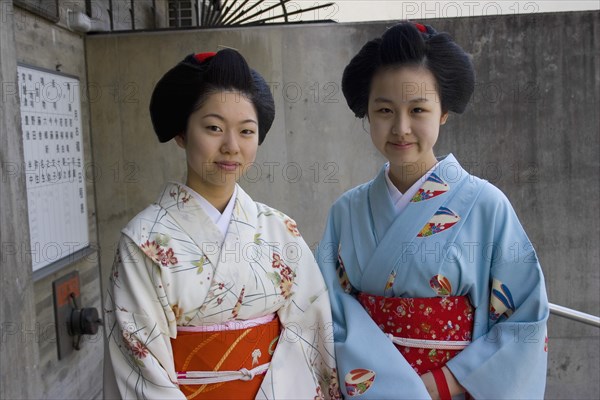 JAPAN, Honshu, Kyoto, "Two Maiko apprentice Geisha wearing patterned kimono, standing outside their house in the Gion District, the neighbourhood where Geisha live, study and perform."