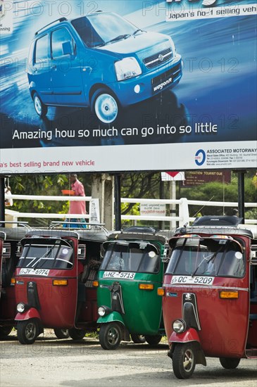 20091062 Tuk Tuks parked underneath advertising billboard Suzuki WagonR. Asia Asian Llankai Sri Lankan  Region - AsiaTransportMedia & CommunicationsDominant RedDominant Blue Jon Hicks 20091062 SRI LANKA  Transport