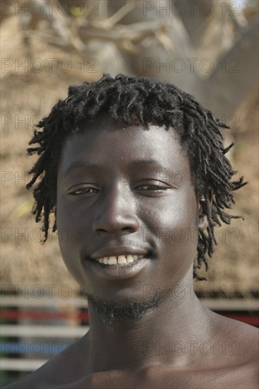 GAMBIA, Western Gambia, Tanji, Tanji coast.  Head and shoulders portrait of smiling young African man with short dreadlocks.
