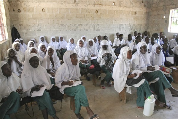 GAMBIA, Western Gambia, Tanji, "Tanji Village.  Muslim students attending a class at the Ousman Bun Afan Islamic school.  Girls sitting seperately from boys, to one side in foreground wearing uniform of white headscarves and green trousers and writing in exercise books."