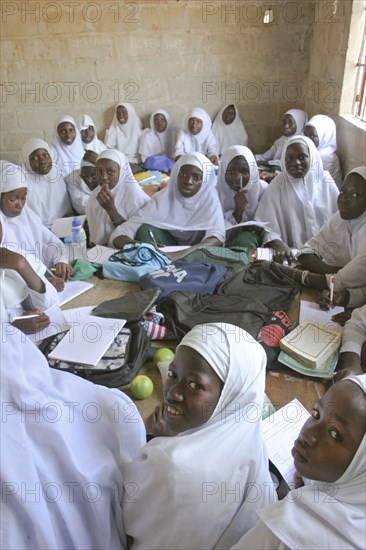 GAMBIA, Western Gambia, Tanji, Tanji Village.  African Muslim girls wearing white headscarves while attending a class at the Ousman Bun Afan Islamic school sitting in groups around desks with bags and books piled in centre.