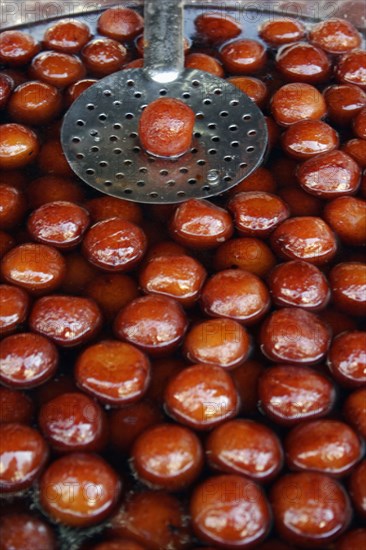 INDIA, Rajasthan, Udaipur, "Indian fried, sweet doughnuts in cooking pot of oil and syrup with single doughnut lifted out on spoon to drain."