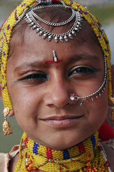 INDIA, Rajasthan, Jodhpur, Portrait of a young Indian girl at Meherangarh Fort wearing nose ring and chain and traditional bead jewelery and black kohl eyeliner.
