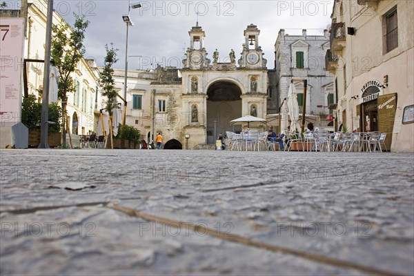 ITALY, Basilicata, Matera, Main square in ancient city of Sassi di Matera or the ‘Stones of Matera’ originating from a prehistoric cave settlement.  UNESCO World Heritage Site.  Cafe bar with outside seating overlooked by church and bell tower.