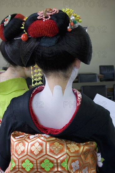 JAPAN, Honshu, Kyoto, Gion District.  Back of Geisha attending a class at Mia Garatso school for Geisha wearing black silk kimono with gold and green obi.  Hair is worn up and fixed with decorative pins and flowers exposing the unpainted nape of the neck which is considered sensuous.  Face and shoulders are painted white.