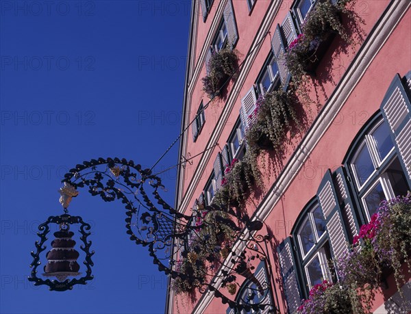 GERMANY, Bavaria, Dinkelsbuhl, Wrought iron cake sign for Cafe Rossimi attached to building facade with shutters on windows and flower boxs