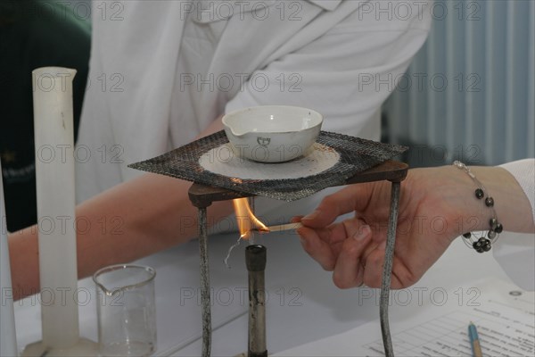 CHILDREN, Education, Secondary, Teacher lighting a bunsen burner prior to it being used for a food technology experiment measuring the evaporation of a salt solution.