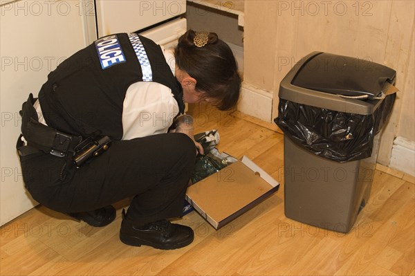 LAW and ORDER, Police, Drugs Raid, Policewoman searching kitchen of residential home during drugs bust.