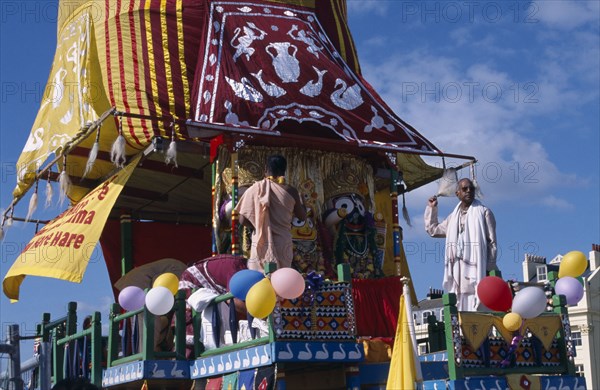 ENGLAND, East Sussex, Brighton, Hare Krishna taking part in a parade on Brighton seafront  with a colourful painted carriage