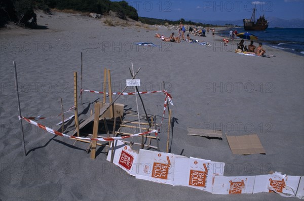 GREECE, Peloponnese, Sea Turtle protection consisting of wood and cardboard forming a cordon around an area on sandy beach near sunbathers