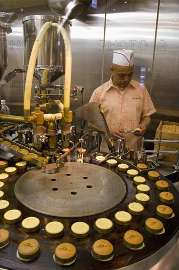 JAPAN, Honshu, Kyoto, Man operating machine making cookies in window of shop.