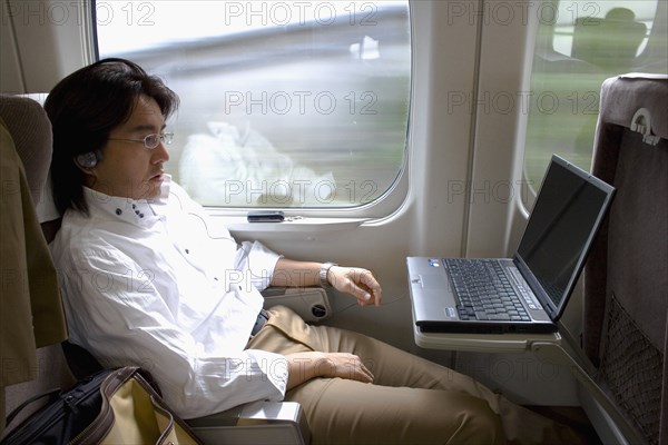 JAPAN, Honshu, Shinkansen train series 700 known as the ‘bullet train’.  Young Japanese man using his laptop with a wireless connection while travelling between Tokyo and Kyoto.