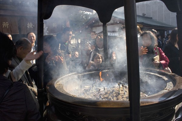 JAPAN, Honshu, Tokyo, Asakusa Kannon or Senso-ji Temple.  Japanese people wafting smoke from incense burner or joukoro over themselves in belief that it will keep them in good health.