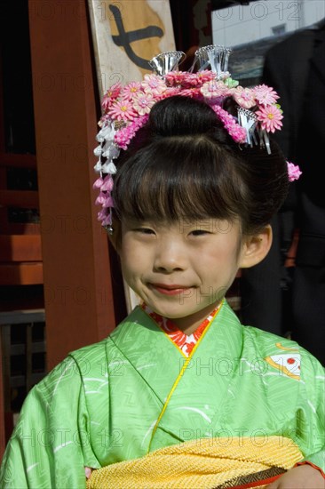 JAPAN, Honshu, Tokyo, Asakusa Kannon or Senso-ji Temple.  Head and shoulders portrait of young Japanese girl wearing pink flower decoration in her hair and green kimono.