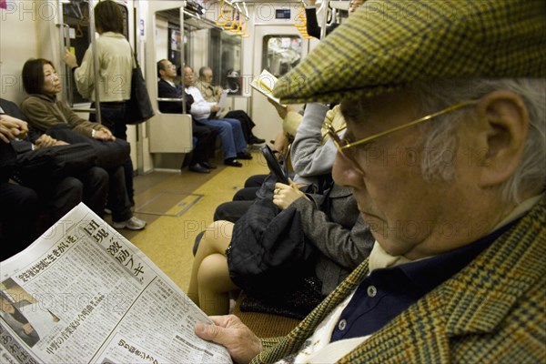 JAPAN, Honshu, Tokyo, Tokyo Metro.  Elderly Japanese man wearing tweed cap and jacket reading a newspaper while travelling on the Tokyo Metro.