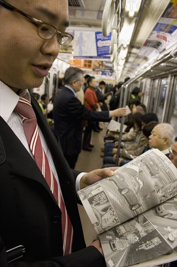 JAPAN, Honshu, Tokyo, Young Japanese man wearing a suit showing the Manga comic he is reading to the photographer while travelling on the Tokyo Metro.