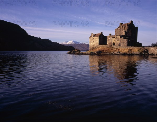 SCOTLAND, North West Highlands, Loch Duich, Eilean Donan Castle.  View of restored castle reflected in Loch Duich and snow covered Beinin na Caillich on the Isle of Skye beyond.