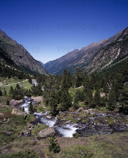 FRANCE, Midi-Pyrenees, Hautes-Pyrenees, Vallee du Lutour.  View north showing ‘u’ shape of eroded glacial valley walls.  Fast flowing river running alongside mountain path with trees on lower slopes.
