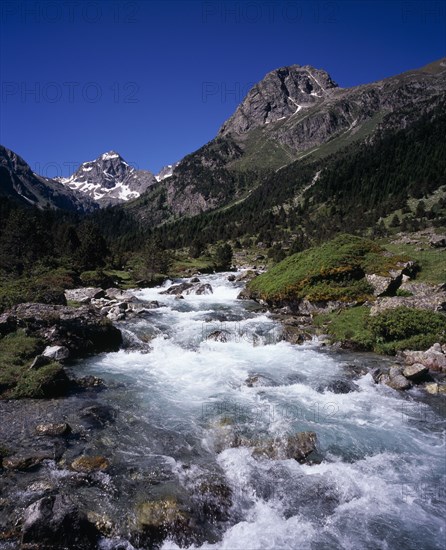 FRANCE, Midi-Pyrenees, Hautes-Pyrenees, Vallee de Lutour looking south with snow covered peak of Pic de Labas 2927 m / 9586 ft and Tuc de Mounges cliff south of Cauterets. Fast flowing river in foreground.