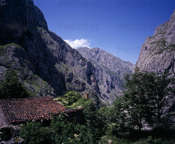 SPAIN, Asturias, Picos de Europa, "View north down Arroyo del Tejo Valley from Bulnes El Castillo with steep sided, eroded limestone cliffs and red tiled roof of ruined barn in foreground."